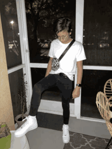 a young man wearing a white shirt and black jeans is sitting on a porch