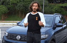 a man in a black shirt with the number 1 on it is standing in front of a blue vw car .