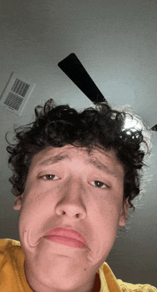 a young man with curly hair making a funny face in front of a ceiling fan