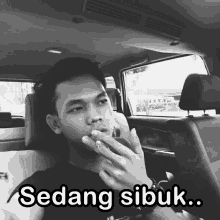 a man smoking a cigarette in the back seat of a car with sedang sibuk written above him