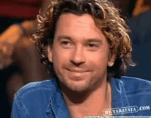 a man with curly hair is smiling for the camera while wearing a blue shirt .