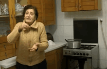 an elderly woman standing in a kitchen with a pot on a stove