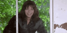 a woman in a leather jacket is smiling while peeking out of a window .