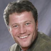a man with a beard and a green jacket is smiling for the camera .