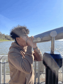 a young man looks through a telescope at a lake