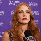 a woman with red hair is holding a microphone in front of a purple wall that says 48th chaplin award