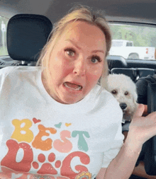 a woman wearing a t-shirt that says best dog is sitting in a car with a small white dog .