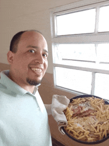 a man holding a pan of food with french fries and meat