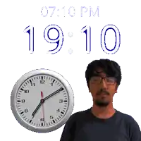 a man wearing glasses stands in front of a clock that says 19:10