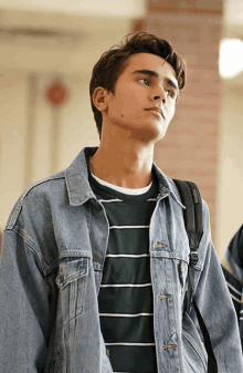 a young man wearing a striped shirt and a denim jacket has a jansport backpack on his back