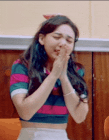 a woman in a striped crop top is praying with her hands folded in front of her face .