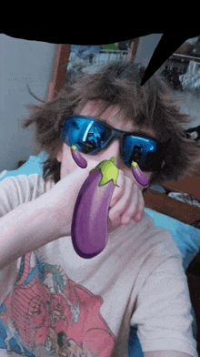 a boy wearing sunglasses and a t-shirt is holding a purple eggplant in front of his face .