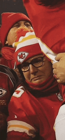 a man wearing a kc hat and glasses is sitting in a stadium