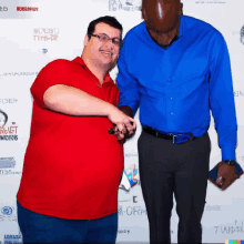 a man in a red shirt stands next to a man in a blue shirt in front of a wall with logos for various companies