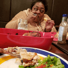 a woman is eating a piece of chicken with a fork and a bottle of dressing in the background