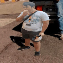 a man is standing on a sidewalk eating a sandwich and holding a bowl of food .