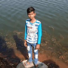 a young boy wearing a blue and white striped shirt stands in front of the water