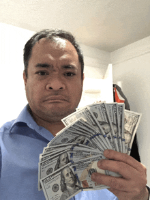 a man in a blue shirt holds a bunch of 100 dollar bills