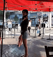 a woman wearing a mask is standing under a red tent in front of a store called los angeles groceries