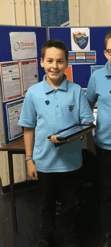 a boy in a blue shirt holding a tablet in front of a childnet international sign