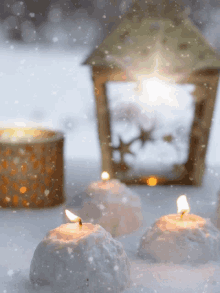 candles in the snow with a lantern in the background and snow falling