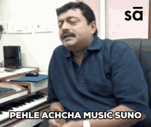 a man sitting in front of a keyboard with the words pehle achcha music suno above him