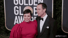 a woman in a red dress and a man in a tuxedo pose on a red carpet in front of a golden globe logo