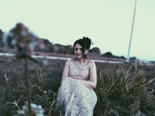 a woman in a white lace dress is sitting in the grass