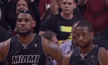 two miami heat basketball players are standing next to each other in front of a crowd during a game .