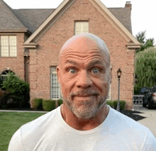 a bald man with a beard is making a face in front of a brick house