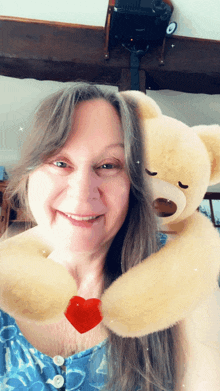 a woman is hugging a teddy bear with a red heart on its arm