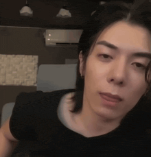 a man with long hair is wearing a black shirt and looking at the camera .