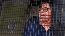 a man with glasses is behind bars in a cage .