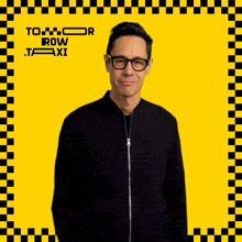 a man wearing glasses and a black jacket stands in front of a yellow and black checkered background that says to row taxi
