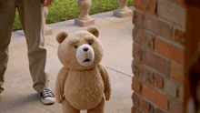 a teddy bear is standing on a sidewalk next to a brick wall