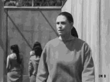 a black and white photo of a woman in a prison uniform standing in front of a group of women .