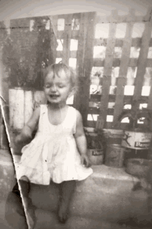 a little girl in a white dress is standing in front of a wooden fence with a can of lemonade in the background