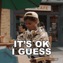 a young man wearing headphones sits at a table with the words " it 's ok i guess " in front of him