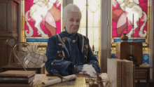 an elderly woman is sitting at a desk in front of a stained glass window holding a piece of paper