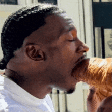 a man in a white shirt is eating a sandwich with his mouth open