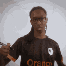 a man wearing glasses and an orange shirt holds a pen