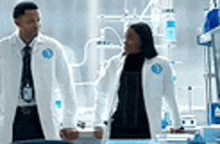 a man and a woman are standing next to each other in a lab talking to each other .