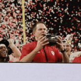 a man in a red shirt with the letter u on it holds a football