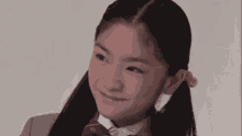 a young girl in a school uniform and bow tie is smiling and looking at the camera .