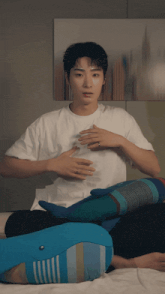 a man in a white t-shirt sits on a bed with a stuffed whale
