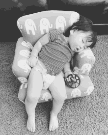 a baby in a diaper sleeping on a chair with elephants on it