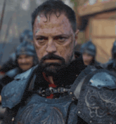 a man with a beard is wearing armor and has a s on his head