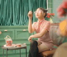 a woman in a cheongsam dress is sitting in a chair with a cup of tea on a table .