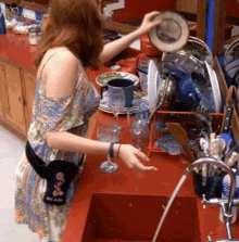 a woman in a dress is washing dishes in a sink with a black bag that says " red claw " on it