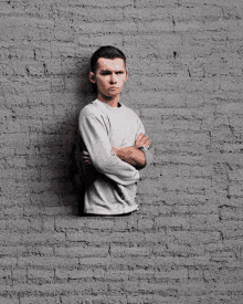 a man with his arms crossed is standing behind a brick wall